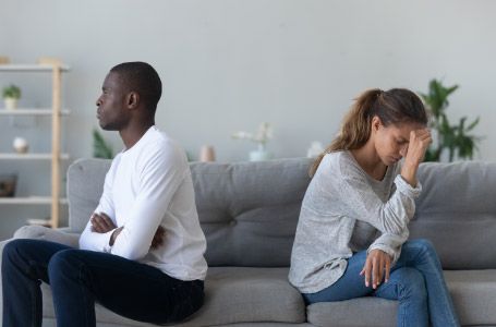 multiracial young couple sit on couch back to back avoid talking after fight